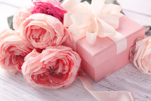 A pink present adorned with a ribbon and surrounded by soft pink roses, suggesting a birthday gift option suitable for all ages